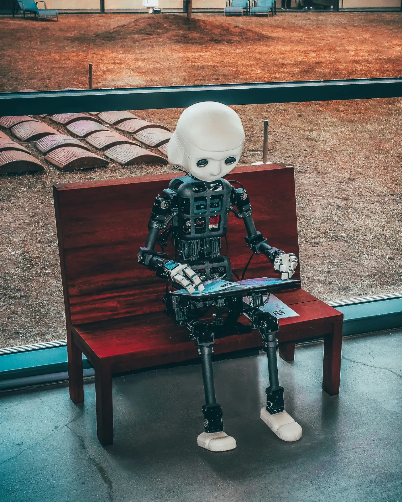 A small humanoid robot sits on a wooden bench reading, illustrating AI interpreting brand messaging